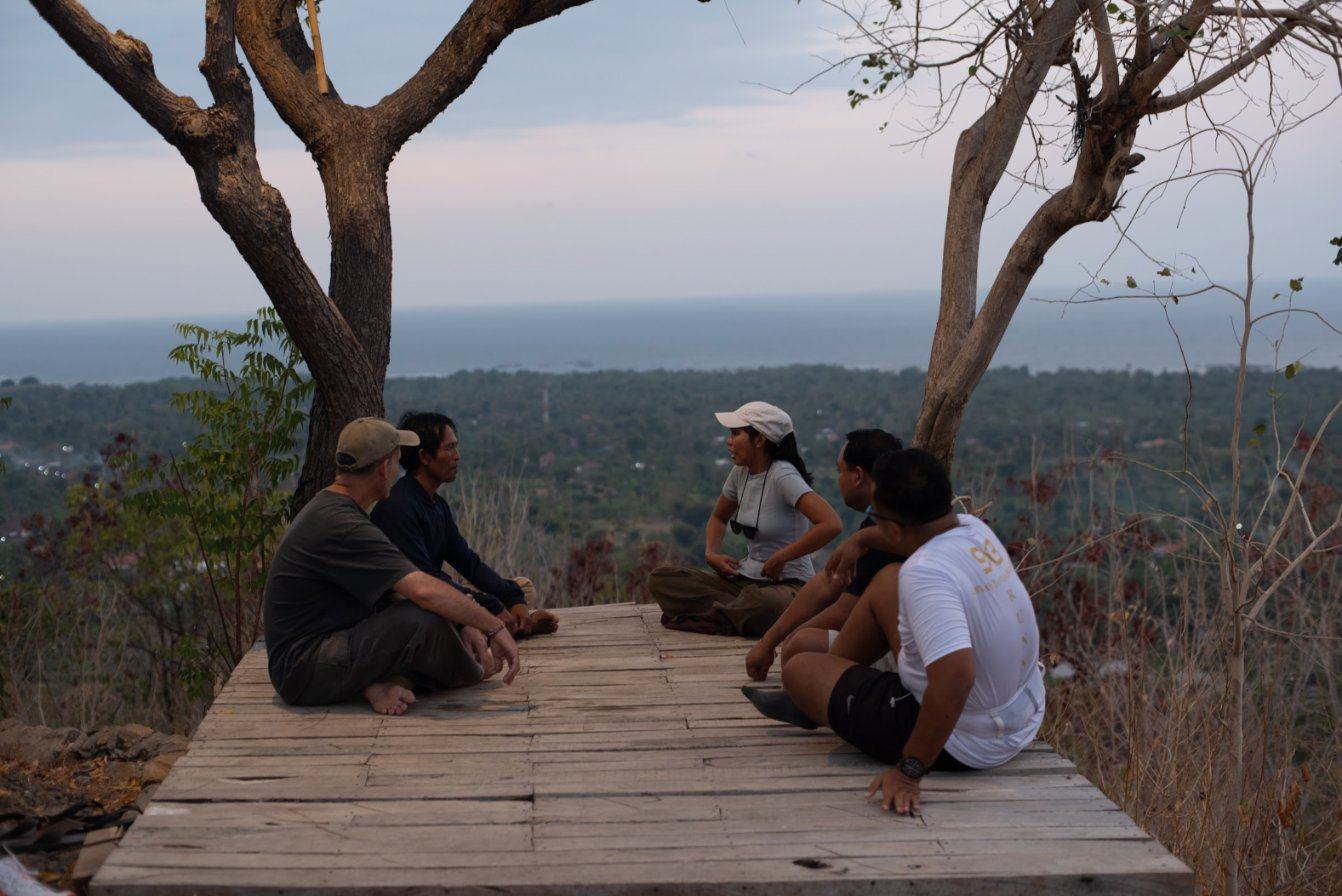 Pilgrims and a guide resting on a wooden deck above the coast at dusk