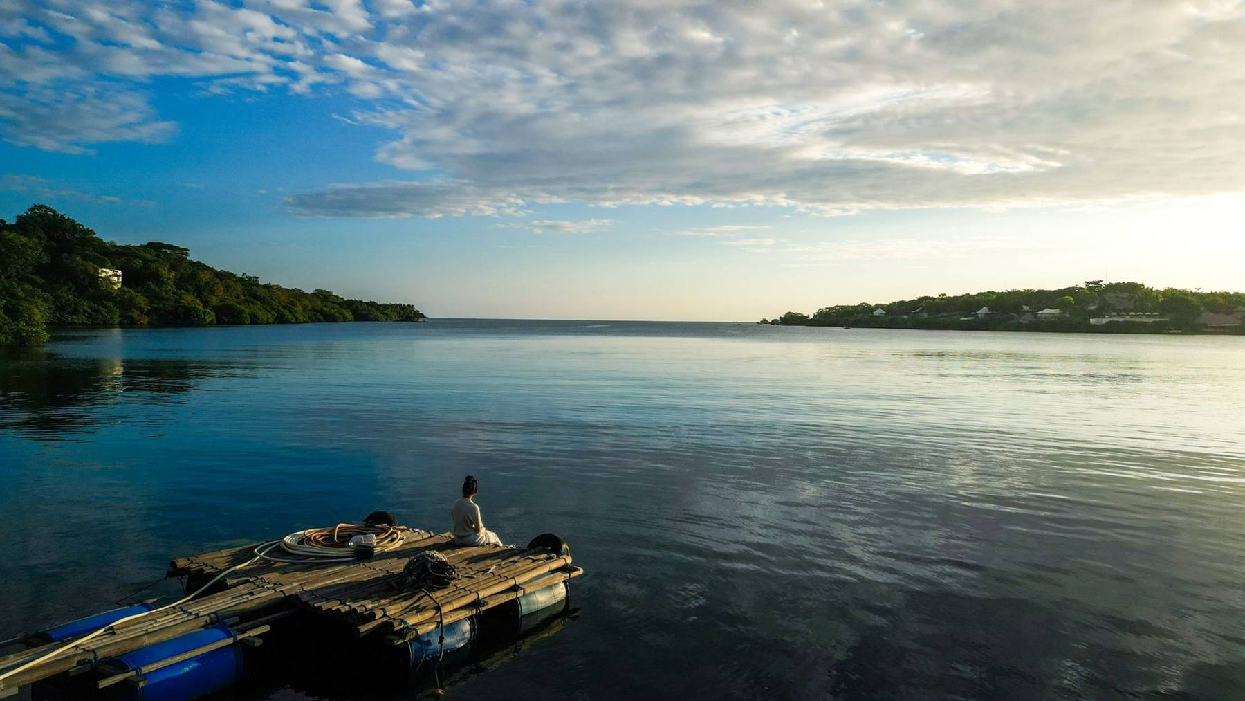 A guide sitting on a bamboo raft in a calm bay at sunrise, northwest Bali