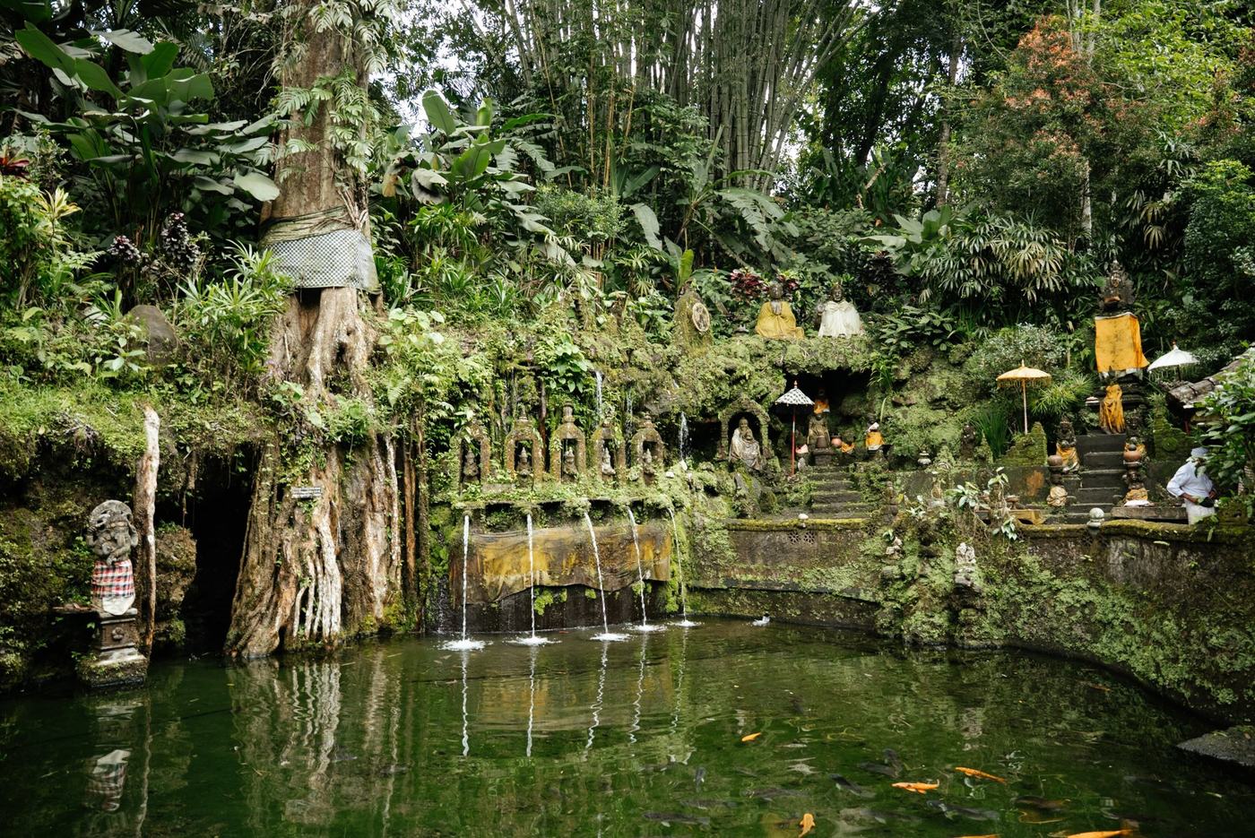 A moss-covered water temple with spouts flowing into a pond under giant trees