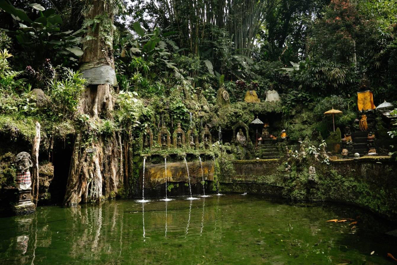 A moss-covered water temple with spouts flowing into a pond under giant trees