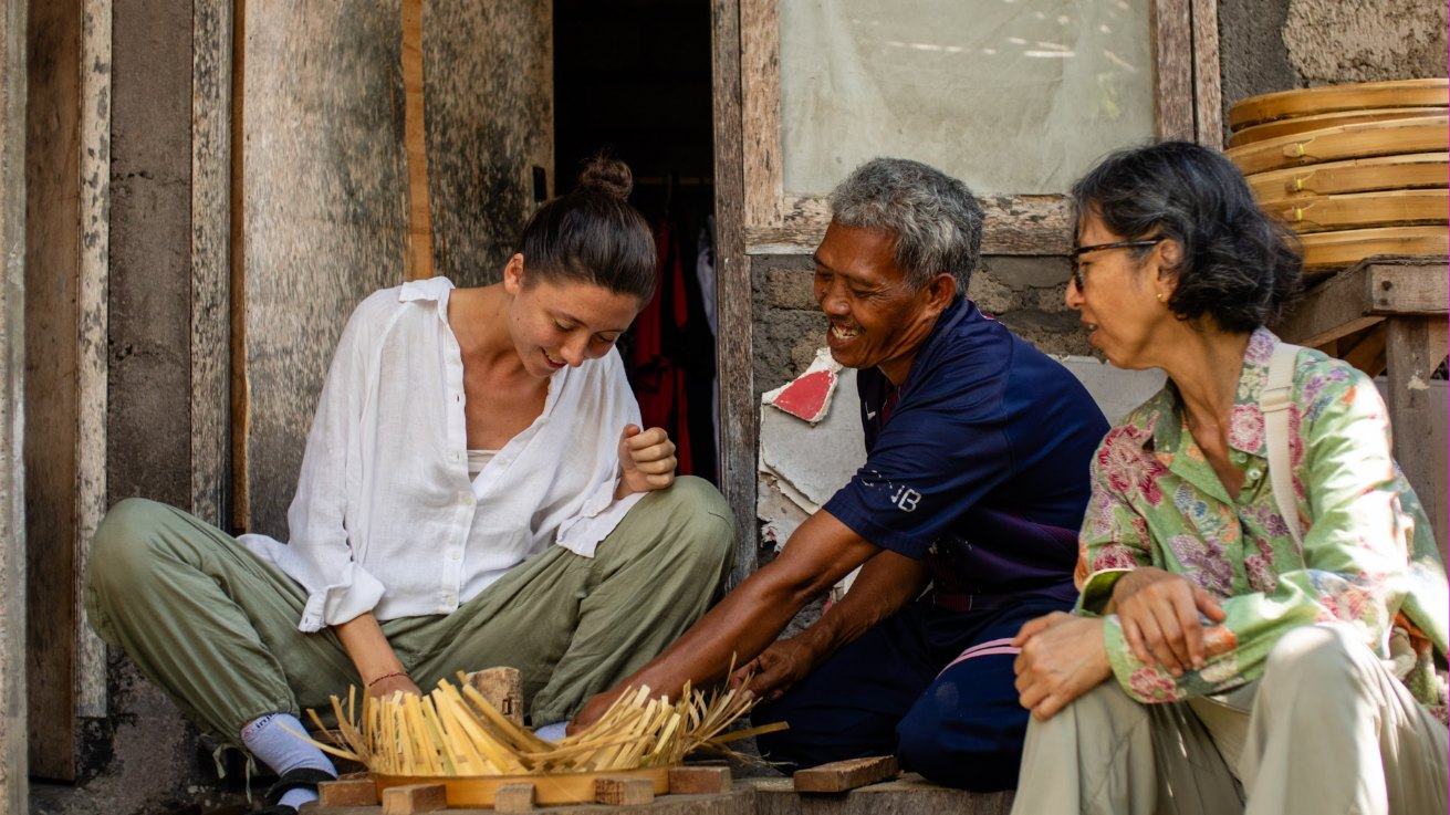A pilgrim weaving bamboo with her hosts on a village doorstep