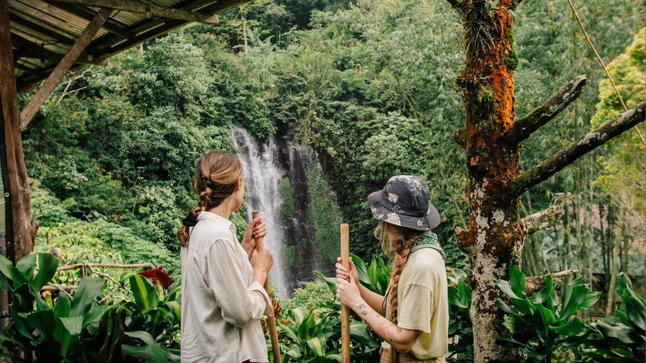 Two pilgrims with bamboo staffs looking at a jungle waterfall