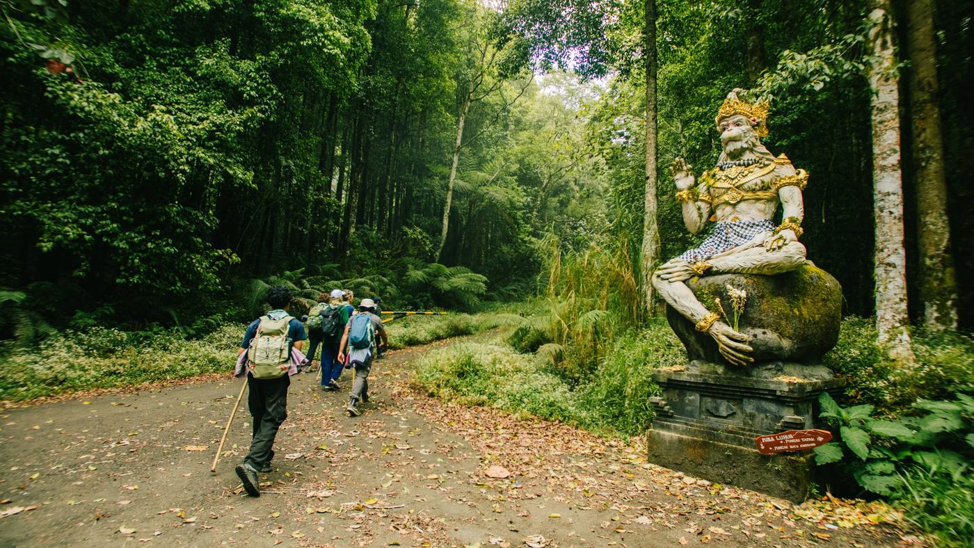 Pilgrims walking a forest road past a Hanuman statue