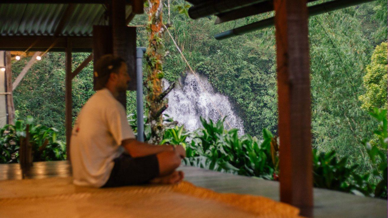 A pilgrim resting on the open-air platform facing the waterfall at dusk