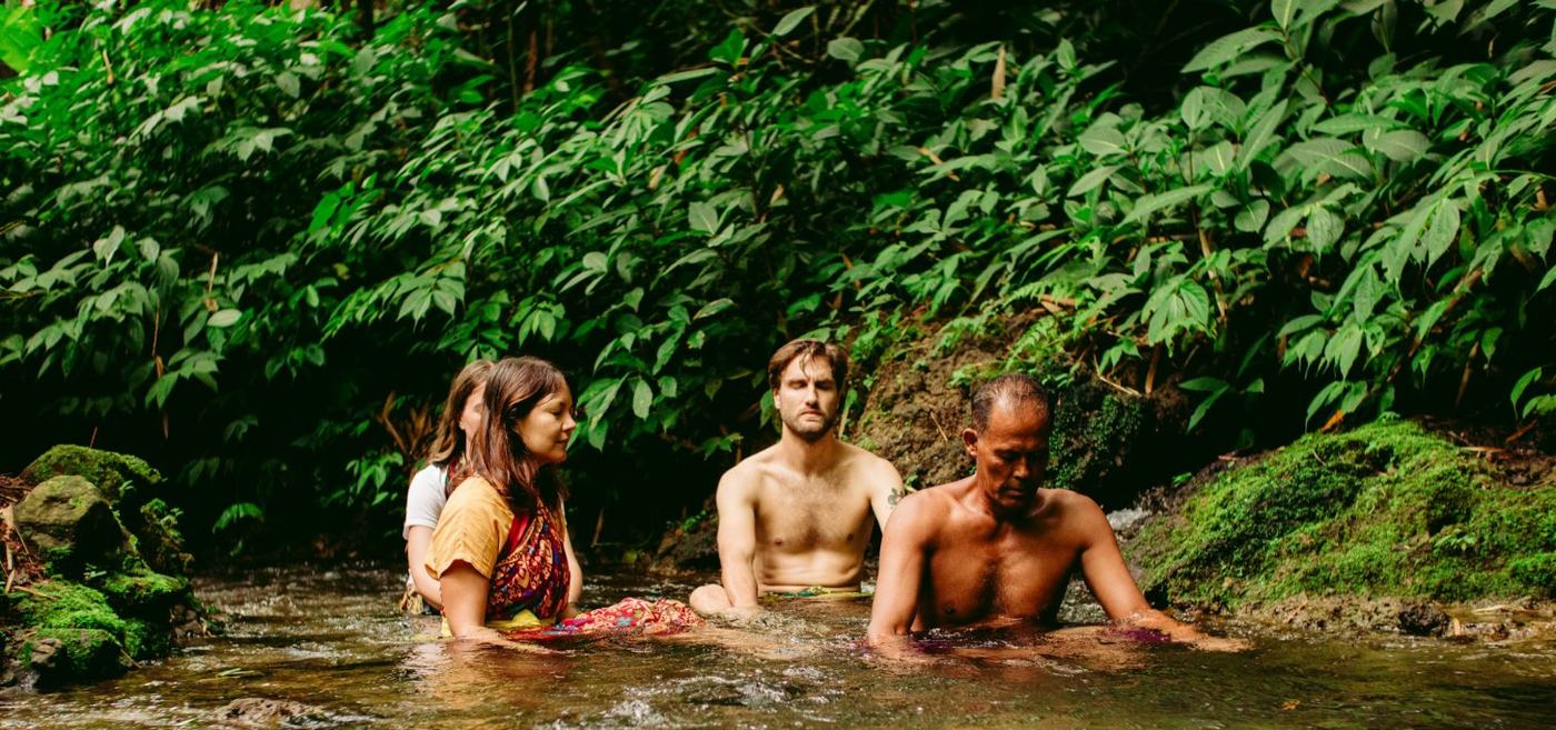 Pilgrims sitting quietly in a forest stream with a local elder